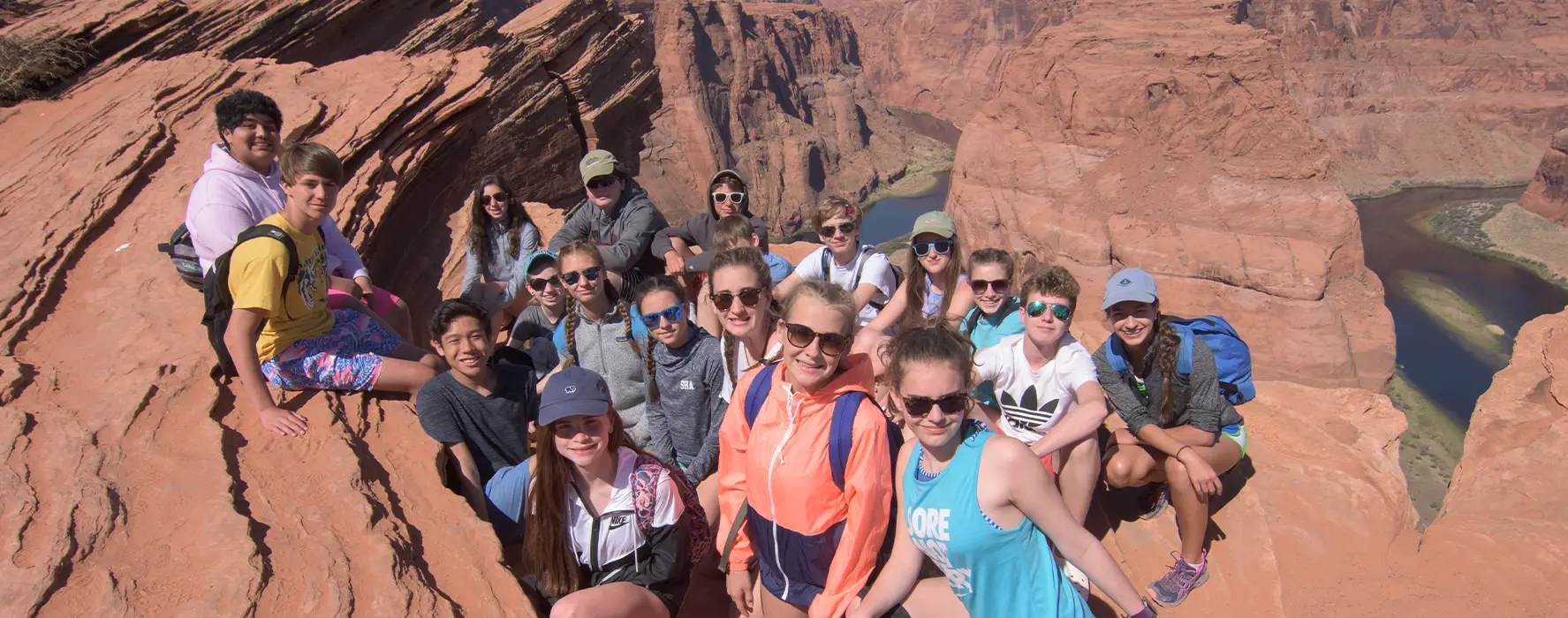 A group of students pose for a photo on the edge of the Grand Canyon with the Colorado River in the background.