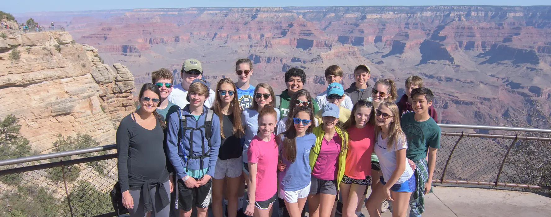 A group of students standing for a photo in front of a fence, with the Grand Canyon in the background.