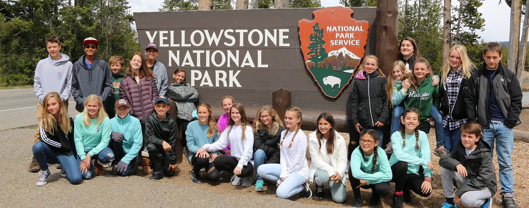 A student group poses in front of the Yellowstone National Park sign.