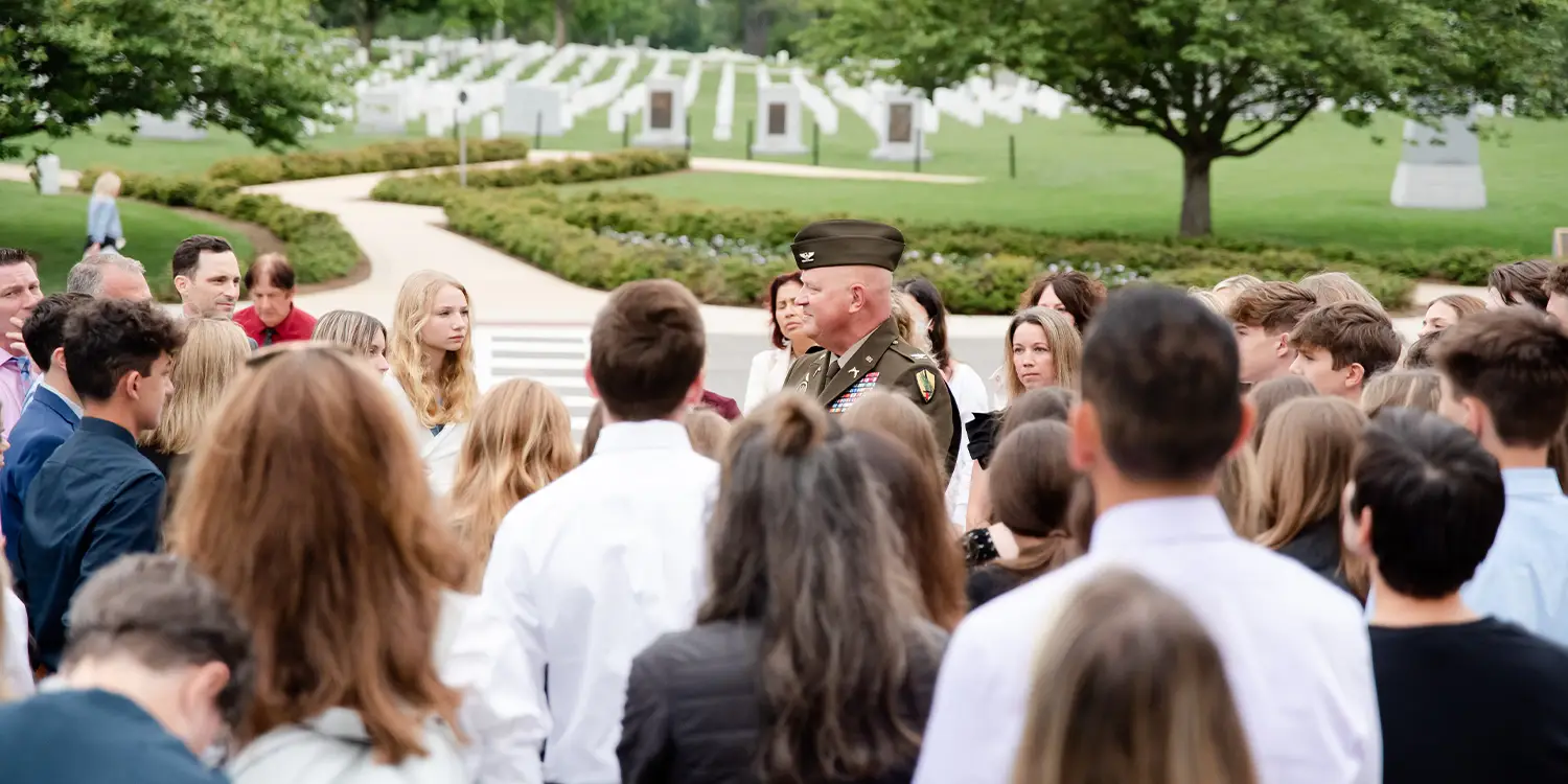 A group of students standing around a man in a military uniform, listening to him speak.